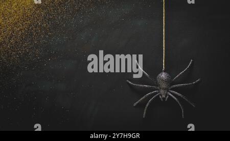 Hanging black glitter spider decoration for halloween, dark grunge gold glitter background, spooky, minimalist night scene, creepy insect suspended in Stock Photo