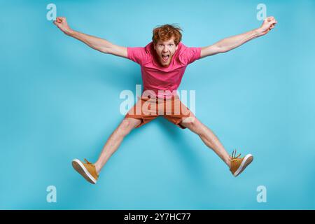 Cheerful young redhead man jumping against blue background Stock Photo