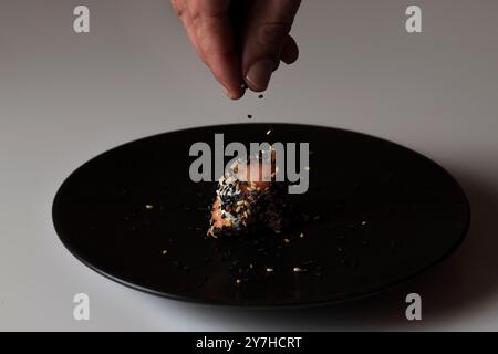 Hand throwing sesame on a salmon roll with cream cheese. Soft focus Stock Photo