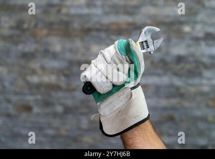 A human hand wearing a tough work glove and holding an adjustable wrench Stock Photo