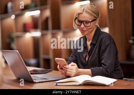 A Professional Woman Engaged in Her Work at a Desk Featuring a Laptop and a Smartphone Stock Photo