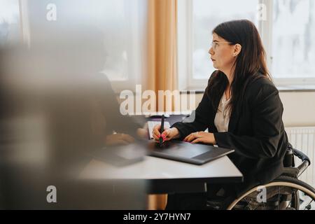 Young businesswoman with physical disability sitting on wheelchair and using digital tablet at office Stock Photo