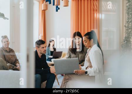 Female business professional discussing with colleagues while using laptop at workplace Stock Photo