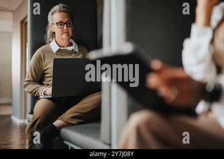 Focused businesswoman using laptop while sitting in booth at office Stock Photo