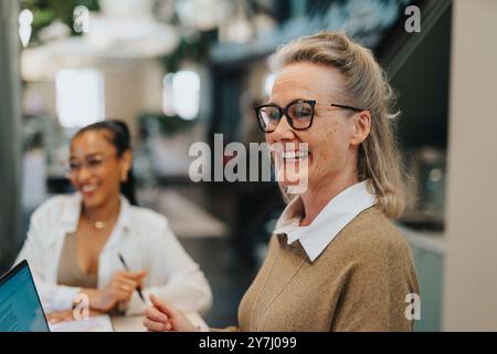 Happy businesswoman wearing eyeglasses working on laptop with coworker in office Stock Photo