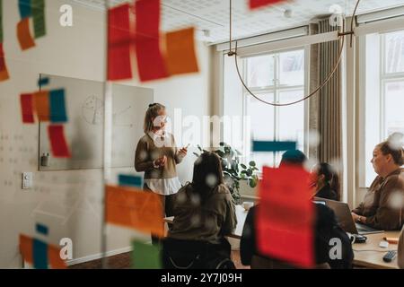 Female business professional explaining ideas to colleagues in meeting room Stock Photo