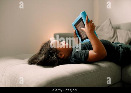 Side view of boy using digital tablet while lying down on sofa at home Stock Photo