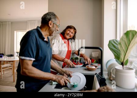 Smiling senior couple assisting each other in doing kitchen chores at home Stock Photo
