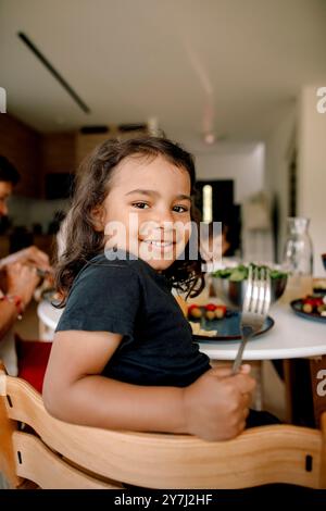 Side view portrait of smiling boy looking over shoulder while holding fork at home Stock Photo