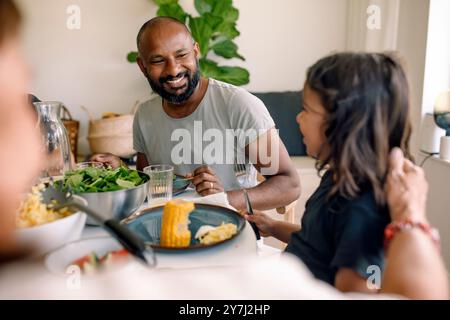 Smiling father looking at son while having lunch at home Stock Photo