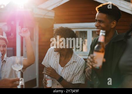 Happy multiracial male friends enjoying drinks while dancing in back yard with friends on sunny day at social gathering Stock Photo