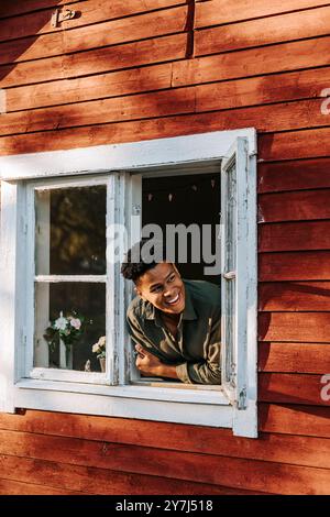 Happy young man leaning and looking through window of house Stock Photo