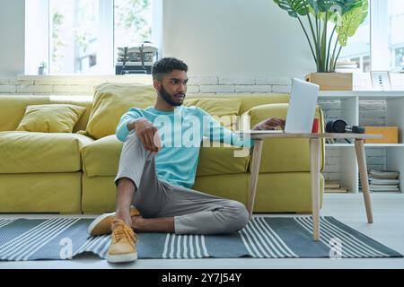 Relaxed African man using laptop while sitting on the floor at home Stock Photo