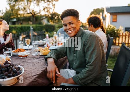 Portrait of happy curly hair young man sitting near dining table in back yard at dinner party Stock Photo