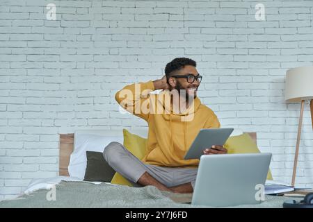 Happy African man using technologies while sitting on the bed at home Stock Photo