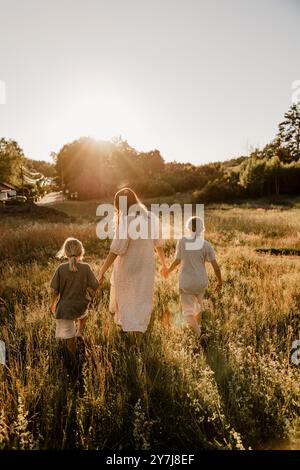 Rear view of mother holding hands of sons and walking on grass in meadow Stock Photo