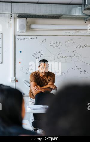 Male teacher leaning on chair while teaching geography in class at junior high school Stock Photo