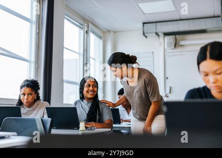 Female teacher assisting student sitting with laptop in classroom at junior high school Stock Photo