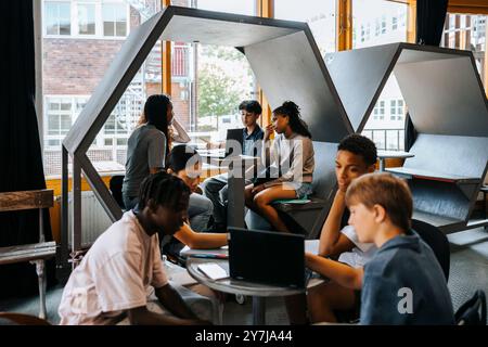 Group of male and female students studying together through laptop while sitting in cafeteria at school Stock Photo