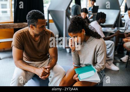 Male professor talking with stressed teenage girl while sitting in cafeteria at school Stock Photo