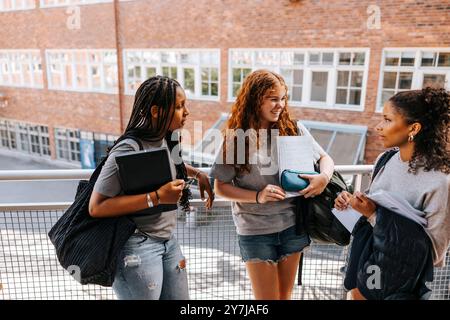 High angle view of multiracial female students discussing with each other while standing near railing in balcony at scho Stock Photo