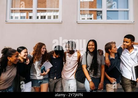 Multiracial male and female junior high students standing side by side near wall of school building Stock Photo