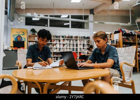 Focused male students studying while sitting near table in library at junior high school Stock Photo