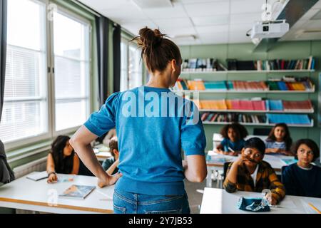 Rear view of female teacher with hand on hip teaching group of elementary students in classroom at school Stock Photo