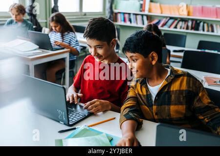 High angle view of boy studying with classmate on laptop while sitting in classroom at elementary school Stock Photo