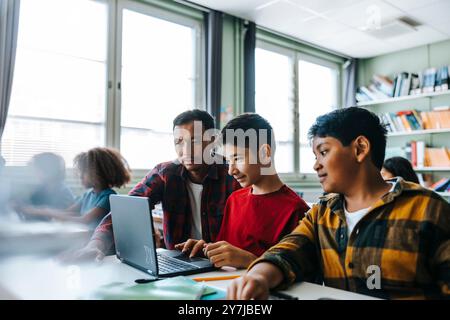 Male teacher assisting student studying on laptop in classroom at elementary school Stock Photo