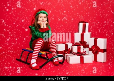 Portrait of her she nice attractive charming tired overwhelmed pre-teen elf Santa Claus apparel look outfit sitting on sled pile stack boxes delivery Stock Photo