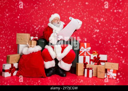 Amazed overwhelmed funky fat overweight plump gray-haired bearded man sitting in chair post office delivery reading wish list letter isolated over Stock Photo