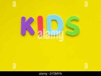 The word Kids from multi-colored letters of the alphabet on a yellow background with copy space. Top view, flat lay. Learning English with colorful le Stock Photo