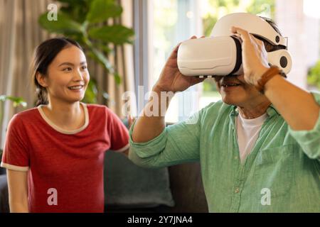 Using VR headset, father exploring virtual reality while daughter smiling nearby Stock Photo