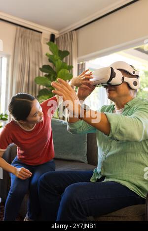 Using VR headset, father exploring virtual reality while daughter assists at home Stock Photo