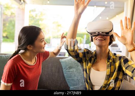Using VR headset, mother enjoying virtual reality experience with daughter watching Stock Photo