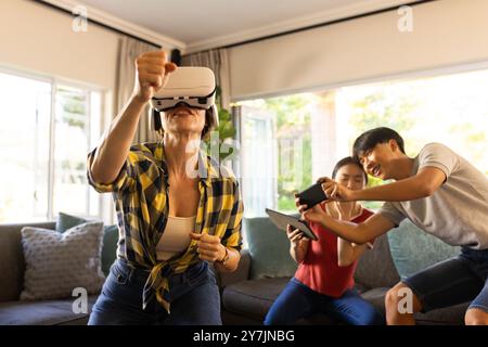Using VR headset, mother playing game while family members watching and laughing Stock Photo