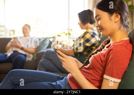 Using smartphones, family members relaxing on couch in living room together Stock Photo