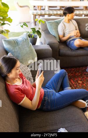 Relaxing on couch, woman using smartphone while man sitting nearby in living room Stock Photo
