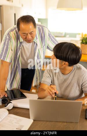 Using laptop and discussing homework, Asian father helping son at home Stock Photo