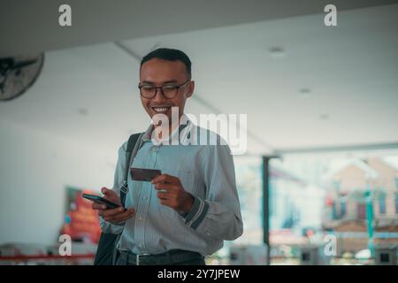 A Young Man Engaged in Using a Smartphone and a Credit Card in a Modern Environment Stock Photo