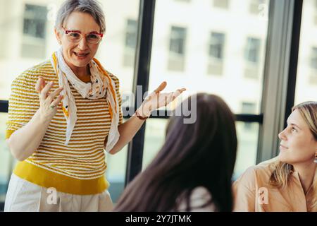 A senior lecturer interacts with college students in a city classroom, promoting an engaging and dynamic educational atmosphere focused on interactive Stock Photo