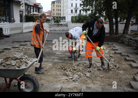 Workers rebuild a sidewalk, one uses a jackhammer, pneumatic drill or demolition hammer, the others use shovels to put pieces of bricks on wheebarrow Stock Photo