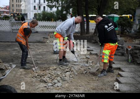 Workers rebuild a sidewalk, one uses a jackhammer, pneumatic drill or demolition hammer, the others use shovels to put pieces of bricks on wheebarrow Stock Photo
