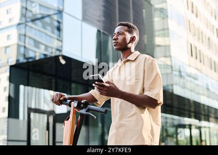 Young Man Standing With E-scooter Outdoors Stock Photo