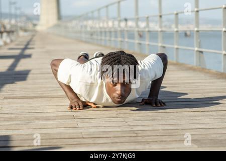 Young man doing push-ups on wooden pier by the water on a sunny day Stock Photo