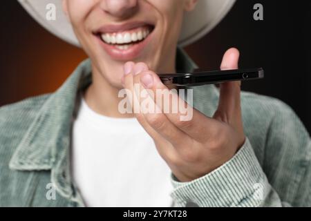 Young man recording voice message via smartphone on dark background, closeup Stock Photo