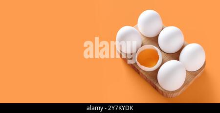 Wooden holder of raw chicken eggs on orange background with space for text Stock Photo