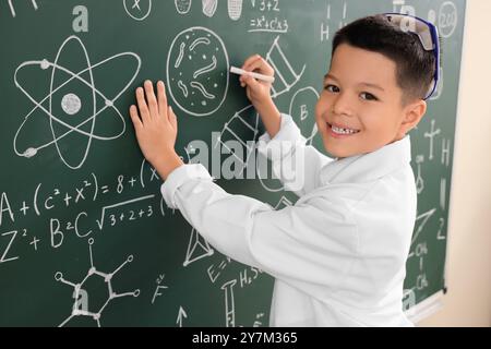 Cute little boy writing on chalkboard at chemistry lesson in classroom Stock Photo