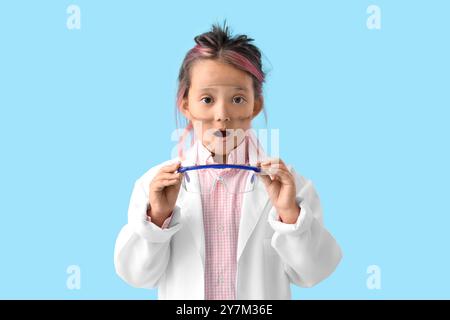 Surprised little girl with dirty face after explosion during chemistry experiment on blue background Stock Photo